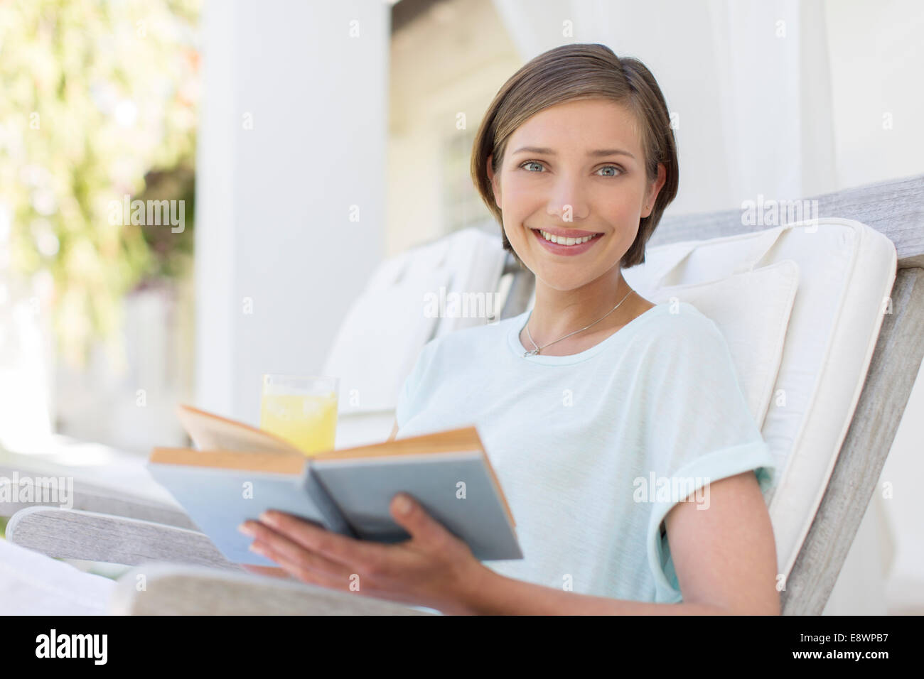 Smiling woman reading book in lawn chair Stock Photo