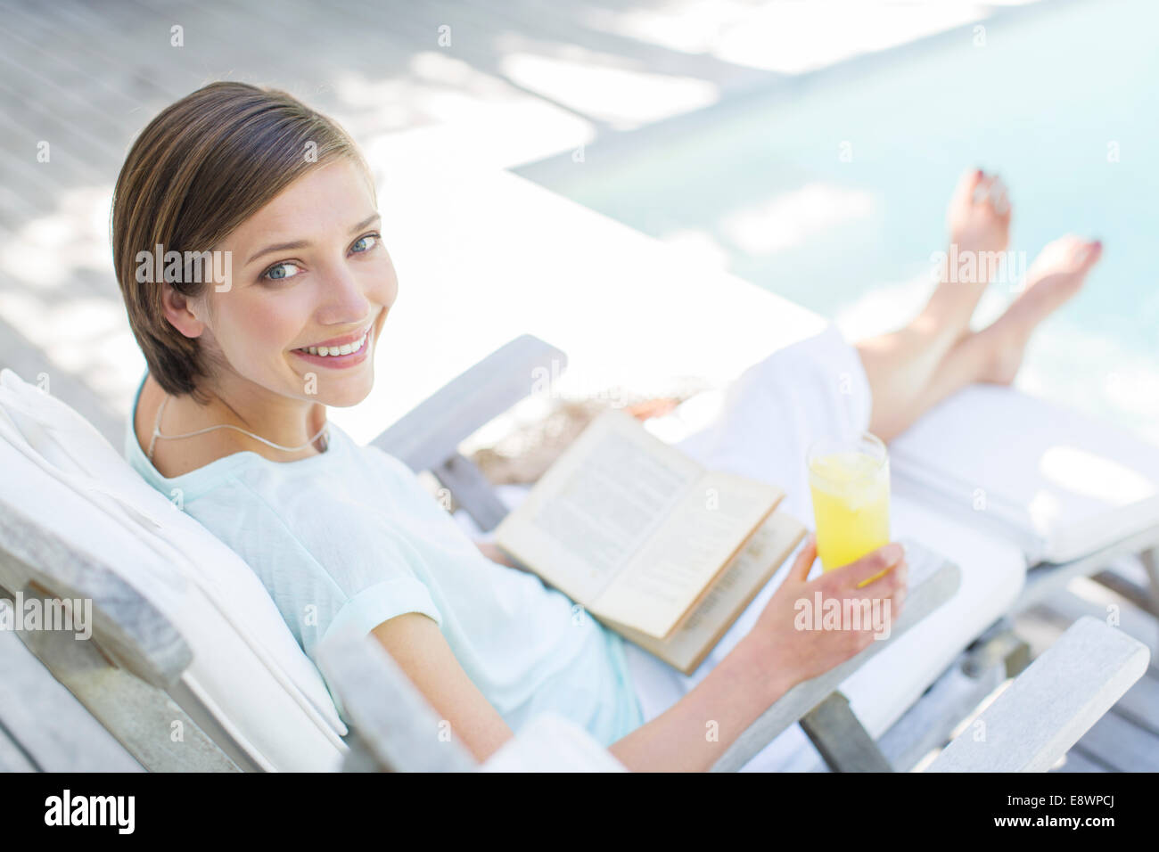High angle view of woman reading and drinking juice by swimming pool Stock Photo