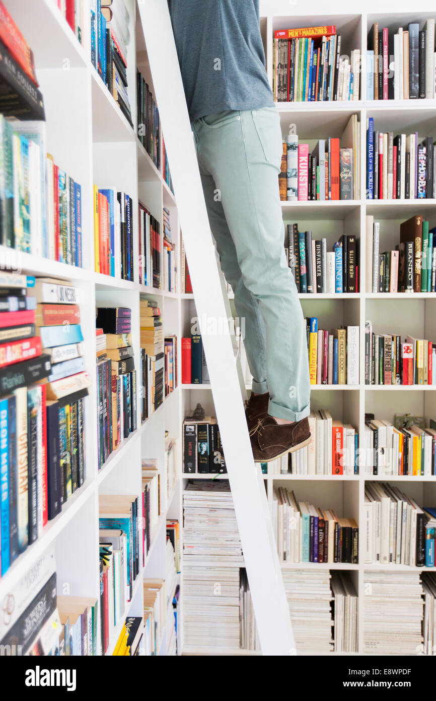 Man standing on ladder to reach books in library Stock Photo