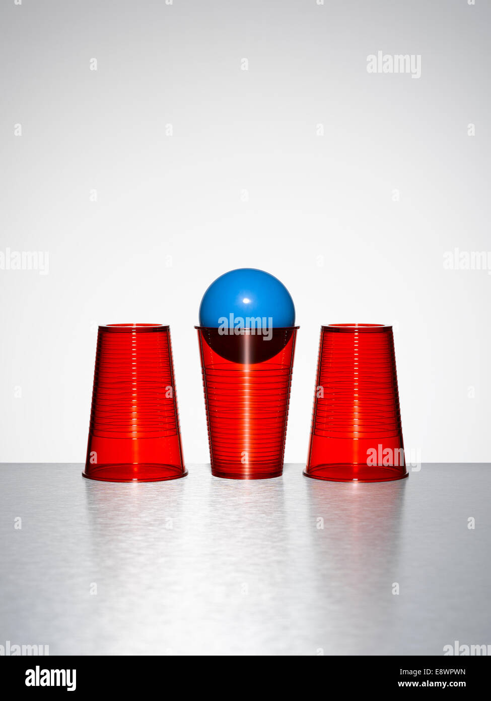 Blue ball in middle of three red cups Stock Photo