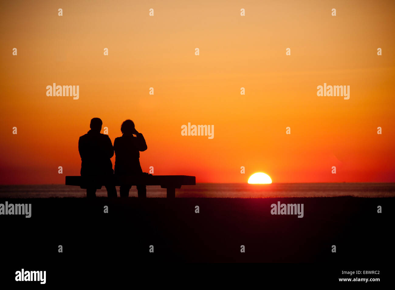 Two people watching the sunrise over the Atlantic Ocean near the Pemaquid, Point Light in Maine, USA Stock Photo