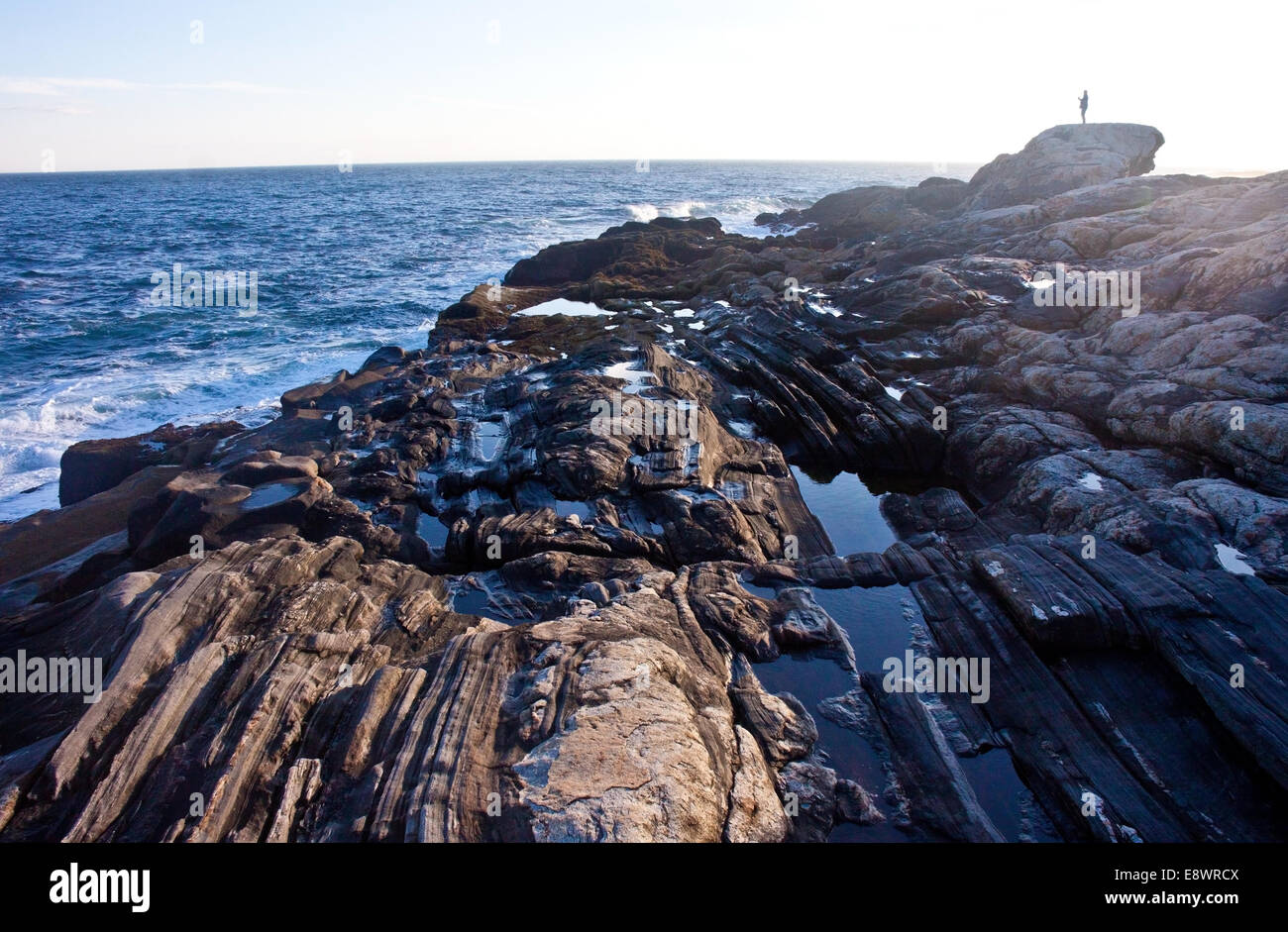 A lone person atop the rocky shoreline near the Pemaquid Point Light in Maine Stock Photo