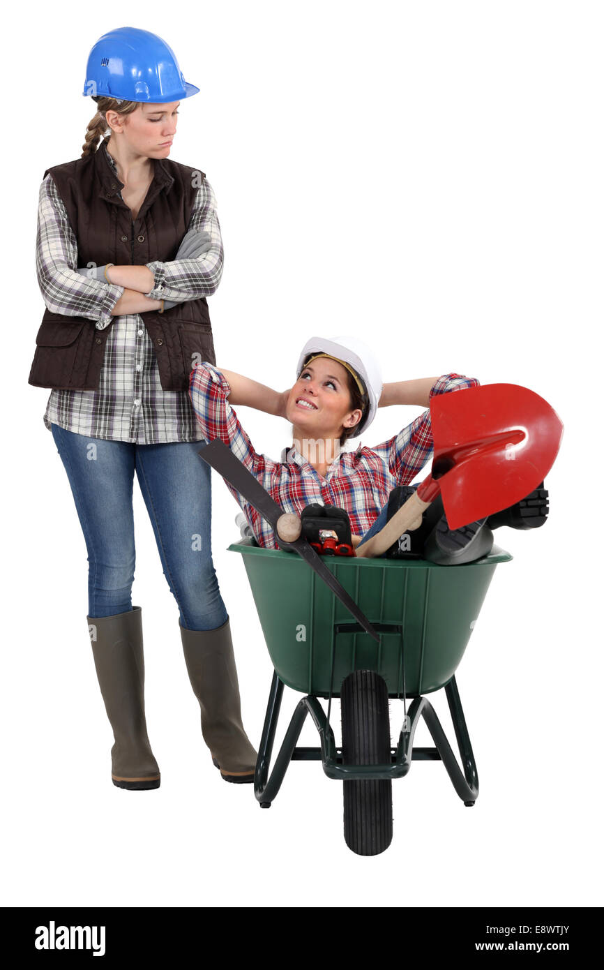 craftswoman accusing her lazy colleague for sitting in a wheelbarrow Stock Photo