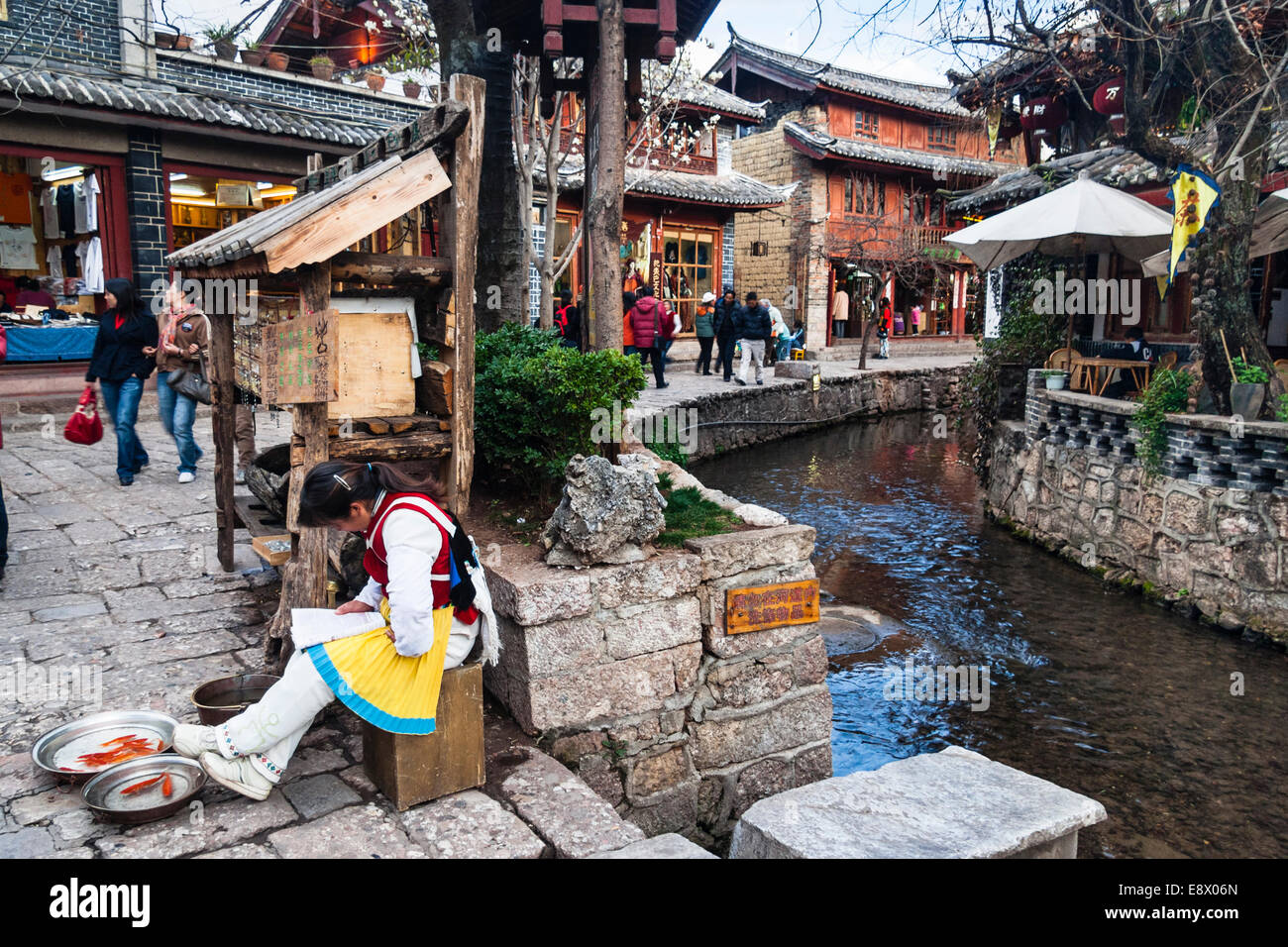 Naxi woman selling red carp by a waterway in old town Lijiang, Yunnan, China Stock Photo