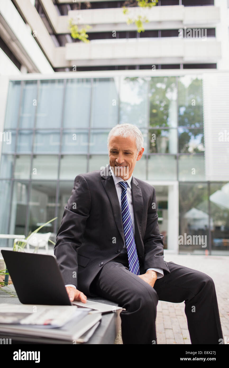 Businessman using laptop on bench outside of office building Stock ...