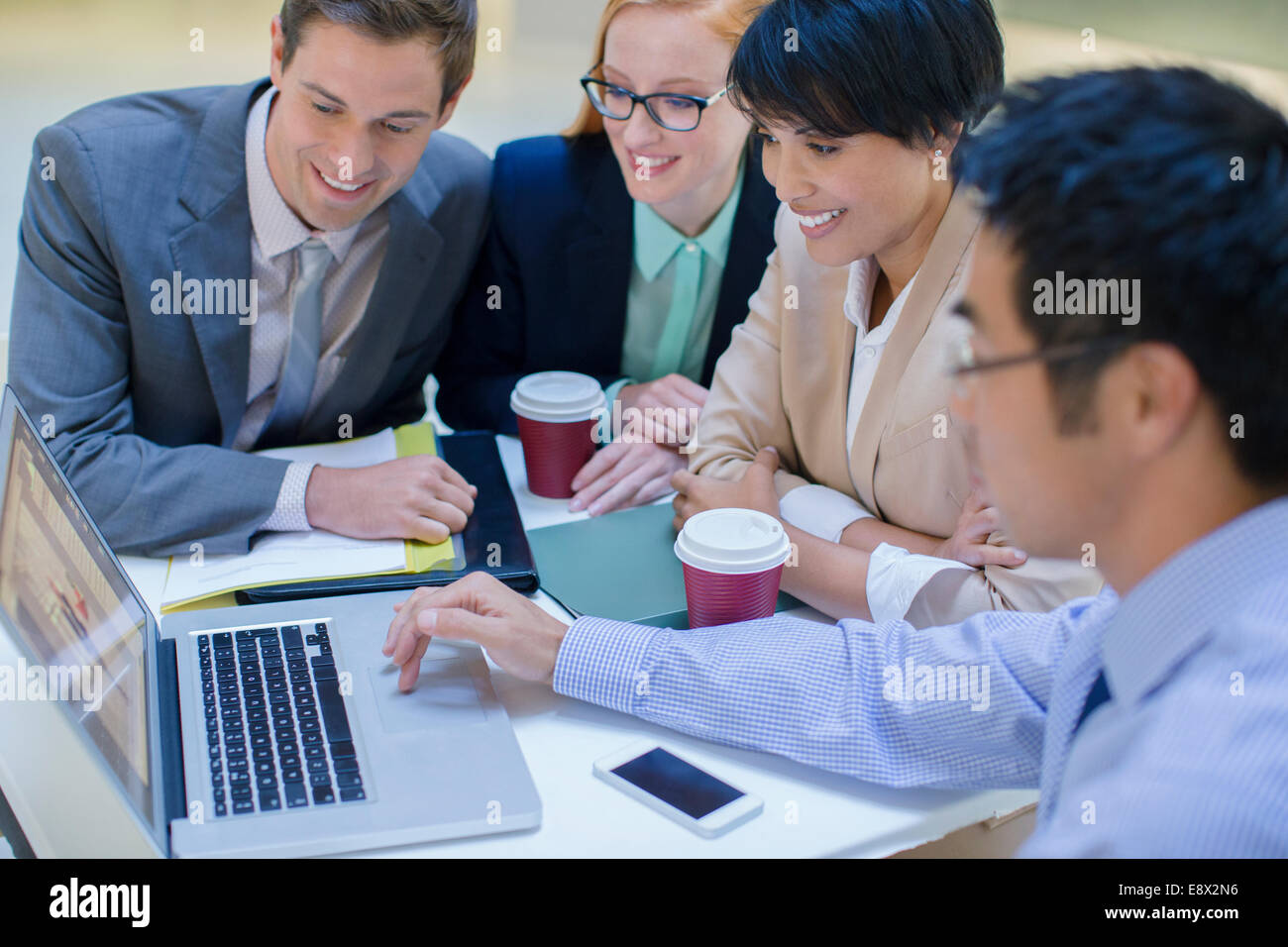 Business people gathered around laptop in office building cafe Stock ...