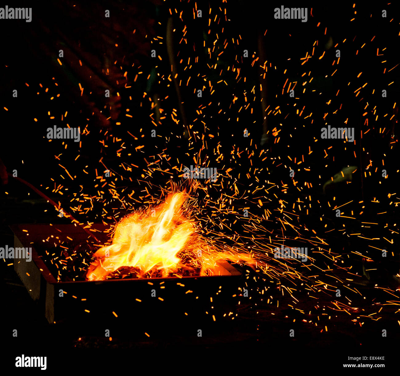 Small BBQ on fire with burning charcoal and flying sparks Stock Photo