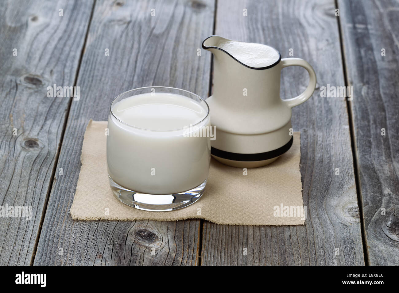 https://c8.alamy.com/comp/E8X8EC/fresh-glass-of-milk-and-pourer-on-rustic-wood-E8X8EC.jpg