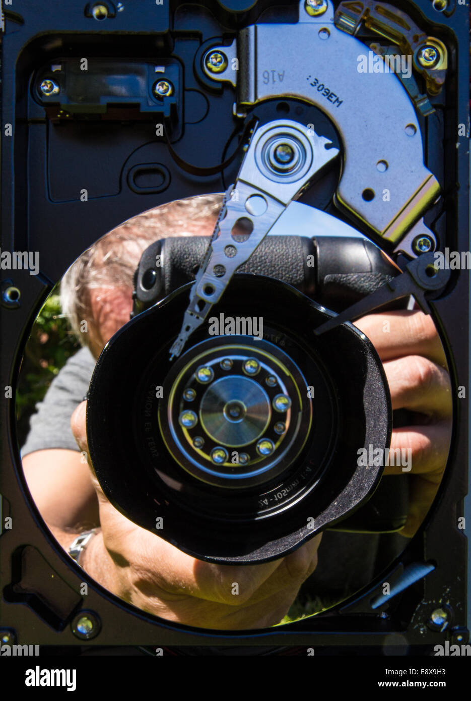 A reflection of a photographer using a camera reflected in a hard drive platen Stock Photo
