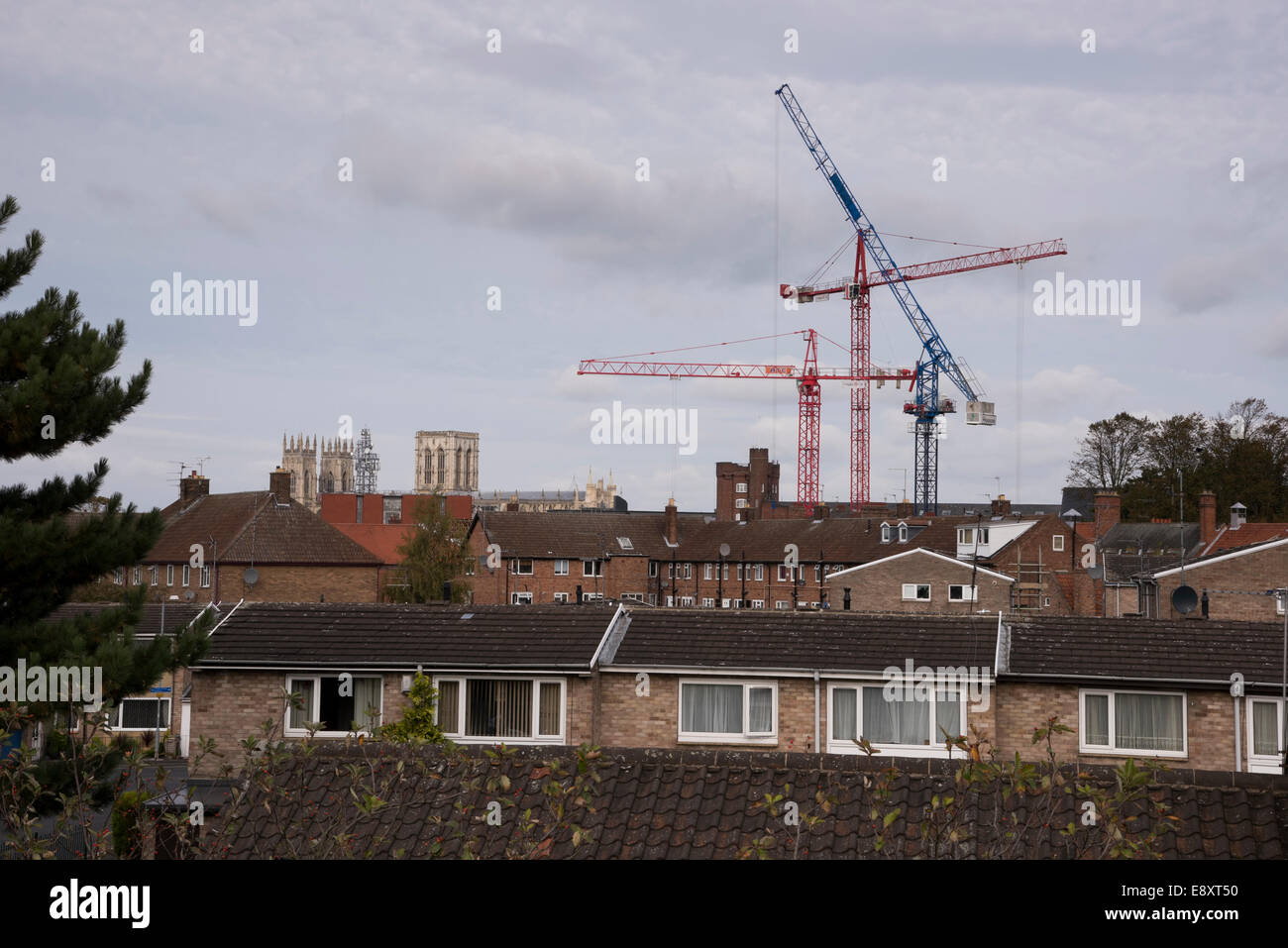 View over rooftops in York, North Yorkshire, England, UK - 3 ancient Minster towers and 3 modern cranes towering over houses in C20th housing estate. Stock Photo
