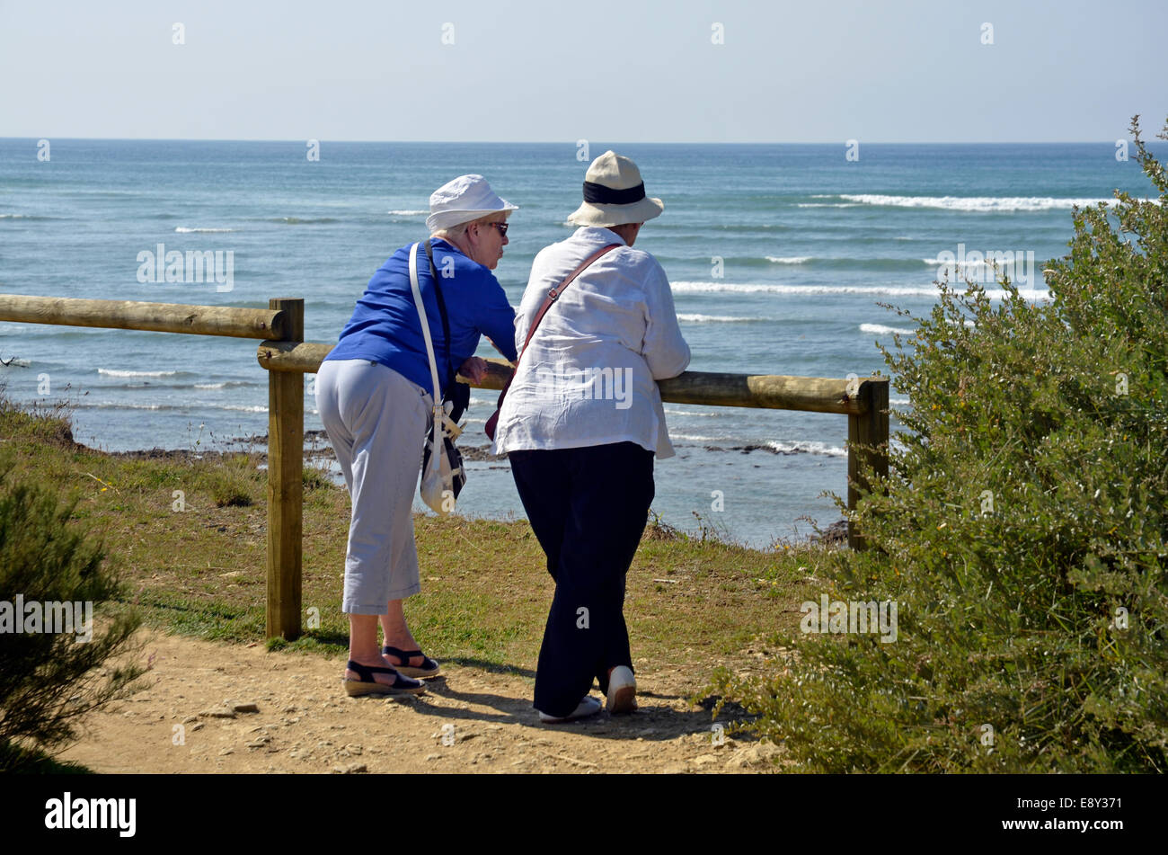 older women leaning on fence looking out to sea Stock Photo