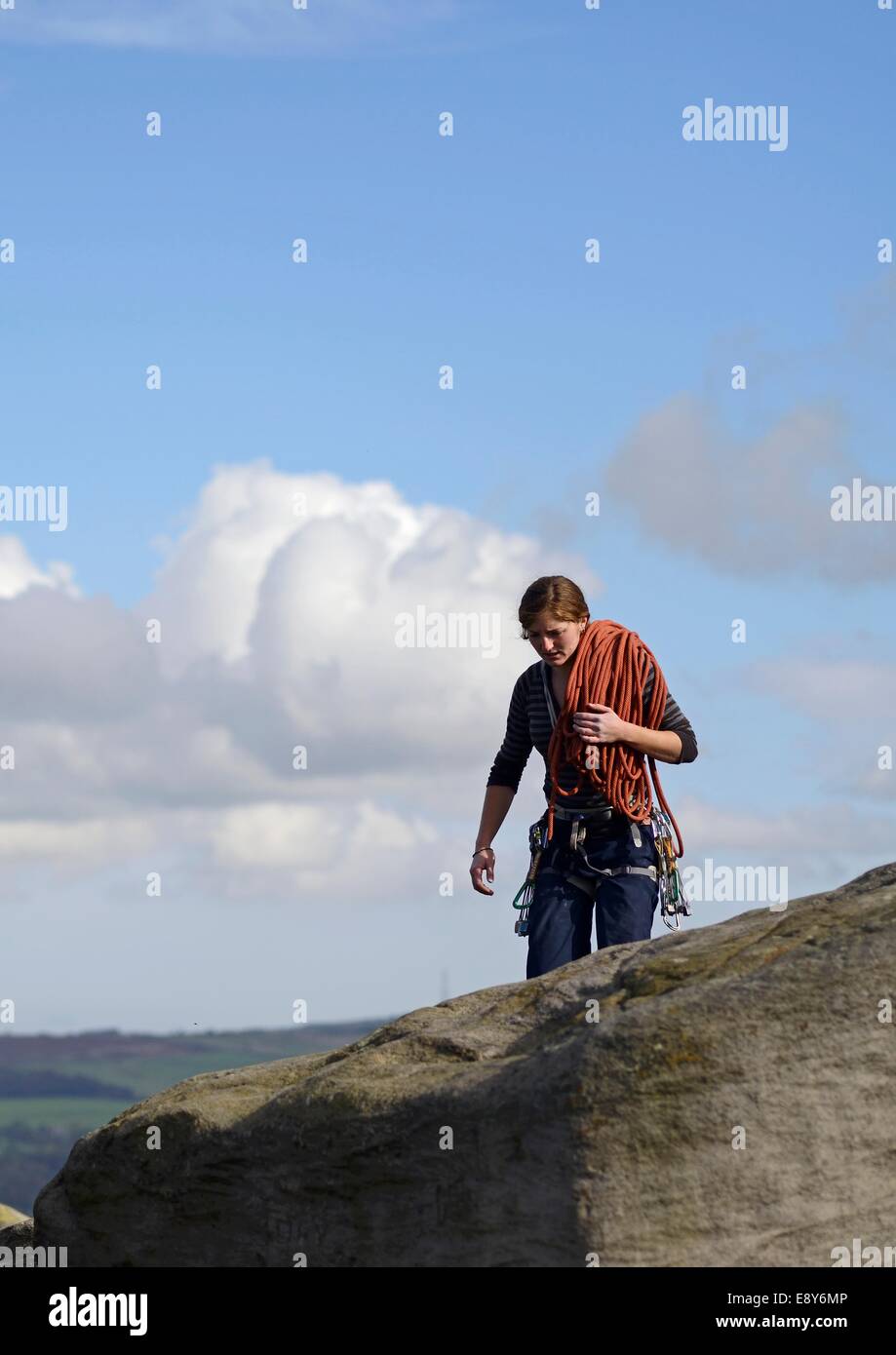 A young woman climber with ropes over her shoulder walking along the top of Cow and Calf rocks on Ilkley Moor, West Yorkshire Stock Photo