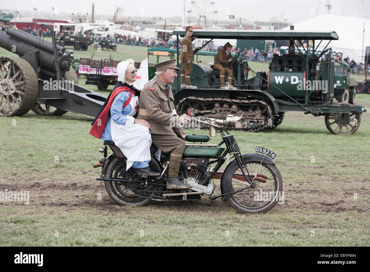 A WW1 medics motorbike being ridden by a British soldiers and Nurse in period uniform, a Holt gun tractor is  in the background. Stock Photo