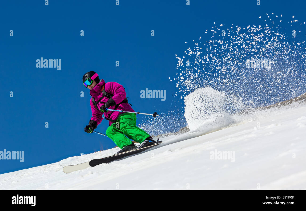 Skier on mountain slope on a clear blue sky. In turn raises the snow dust. Stock Photo