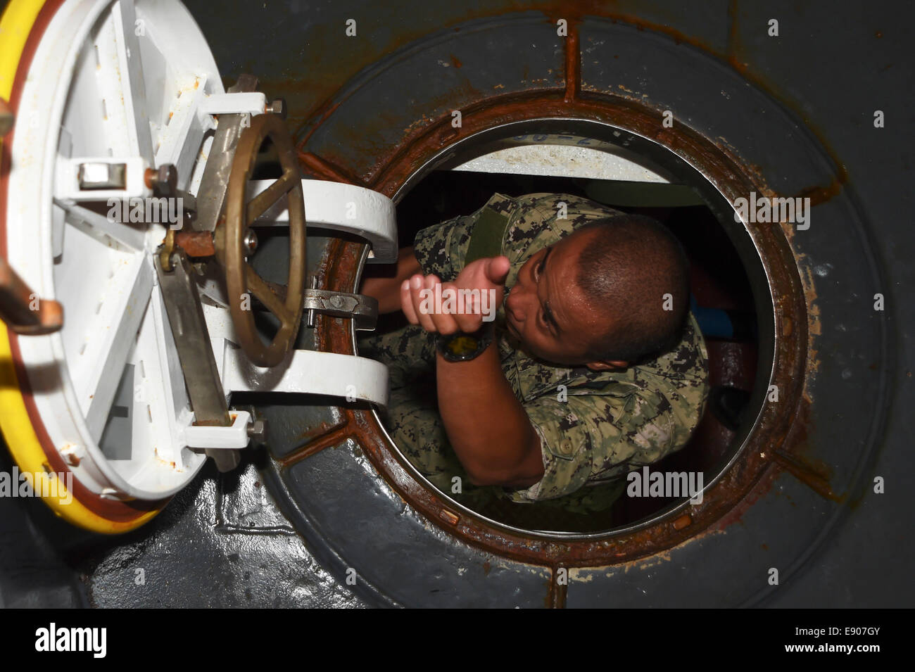 U.S. Navy Machinist's Mate 1st Class Ariel Ancheta climbs out of a hatch while conducting a tour of a U.S. Navy landing craft, utility assigned to Naval Beach Unit 7 for Philippine navy officers while aboard the amphibious assault ship USS Peleliu (LHA 5) Stock Photo