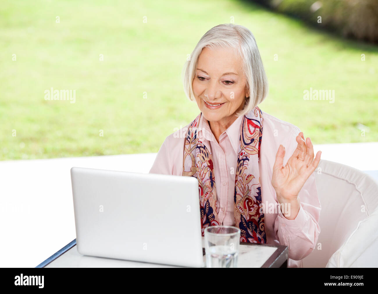 Senior Woman Waving While Video Conferencing On Laptop Stock Photo