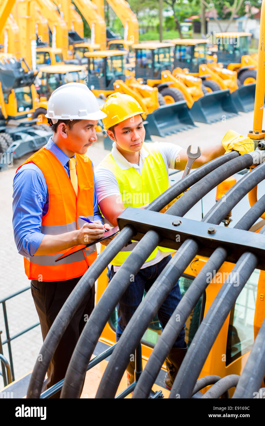 Asian motor mechanic discussing with engineer task list in construction machine workshop Stock Photo