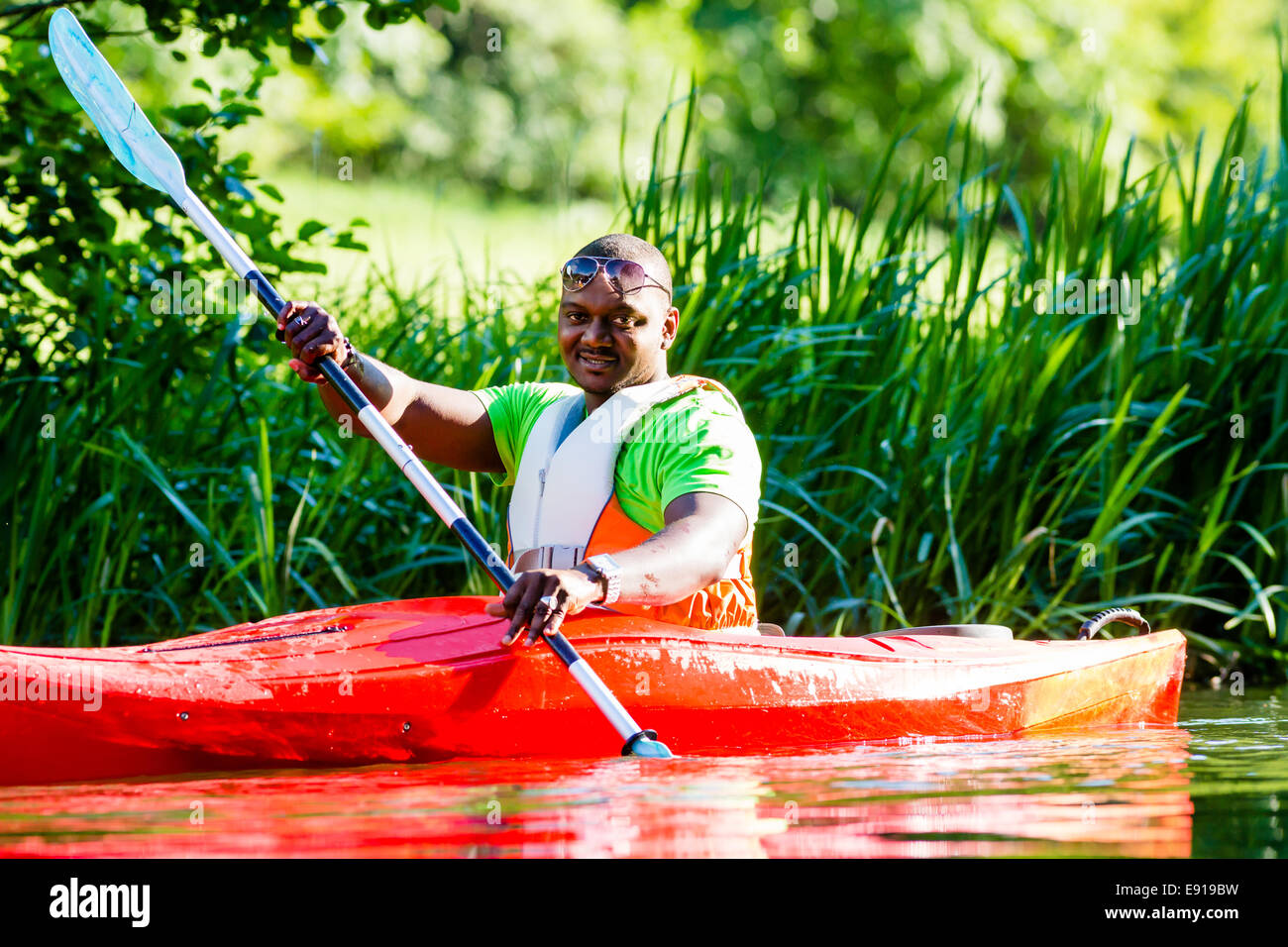 African Man paddling with canoe on forest river Stock Photo