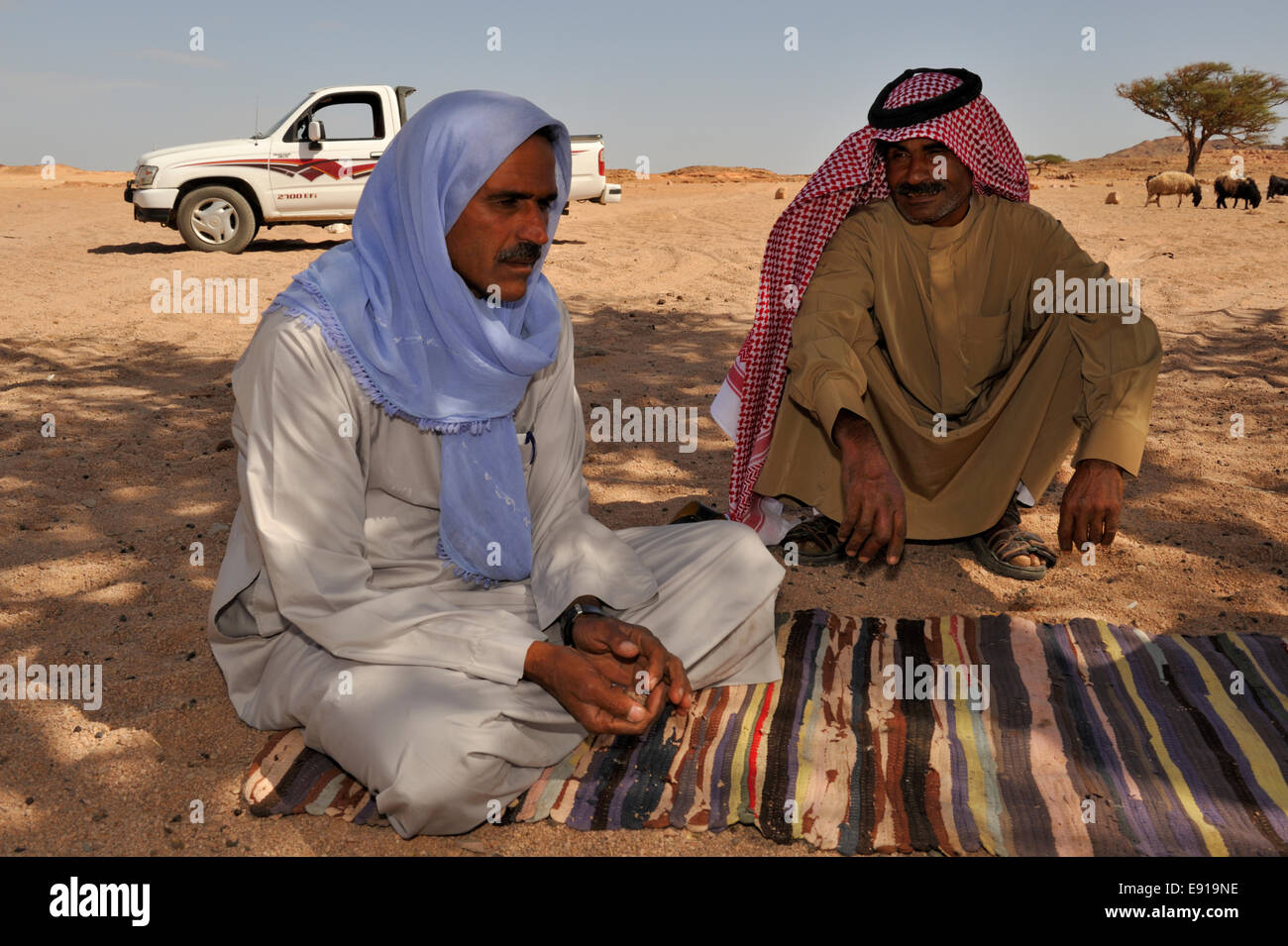 Two Bedouin Arab men relaxing on traditional blanket in shadow of
