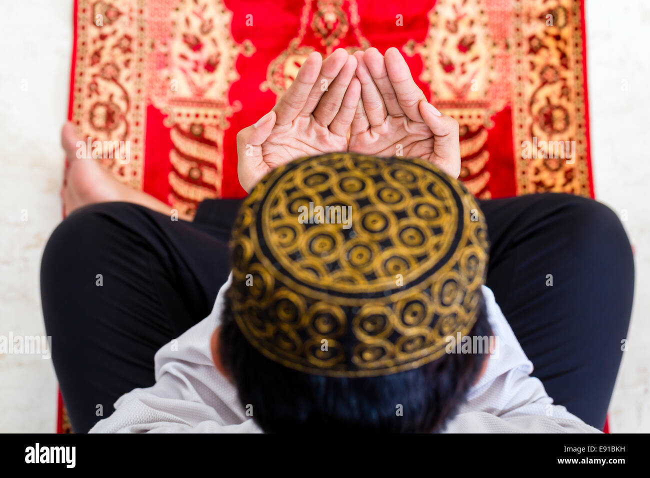 Asian Muslim man praying on carpet wearing traditional dress Stock Photo