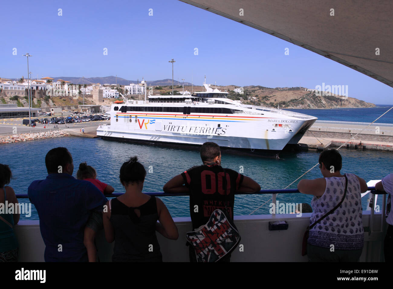 Tarifa Spain ferry passengers watch as they depart Tarifa port passing a moored Virtu Ferries ferry Stock Photo