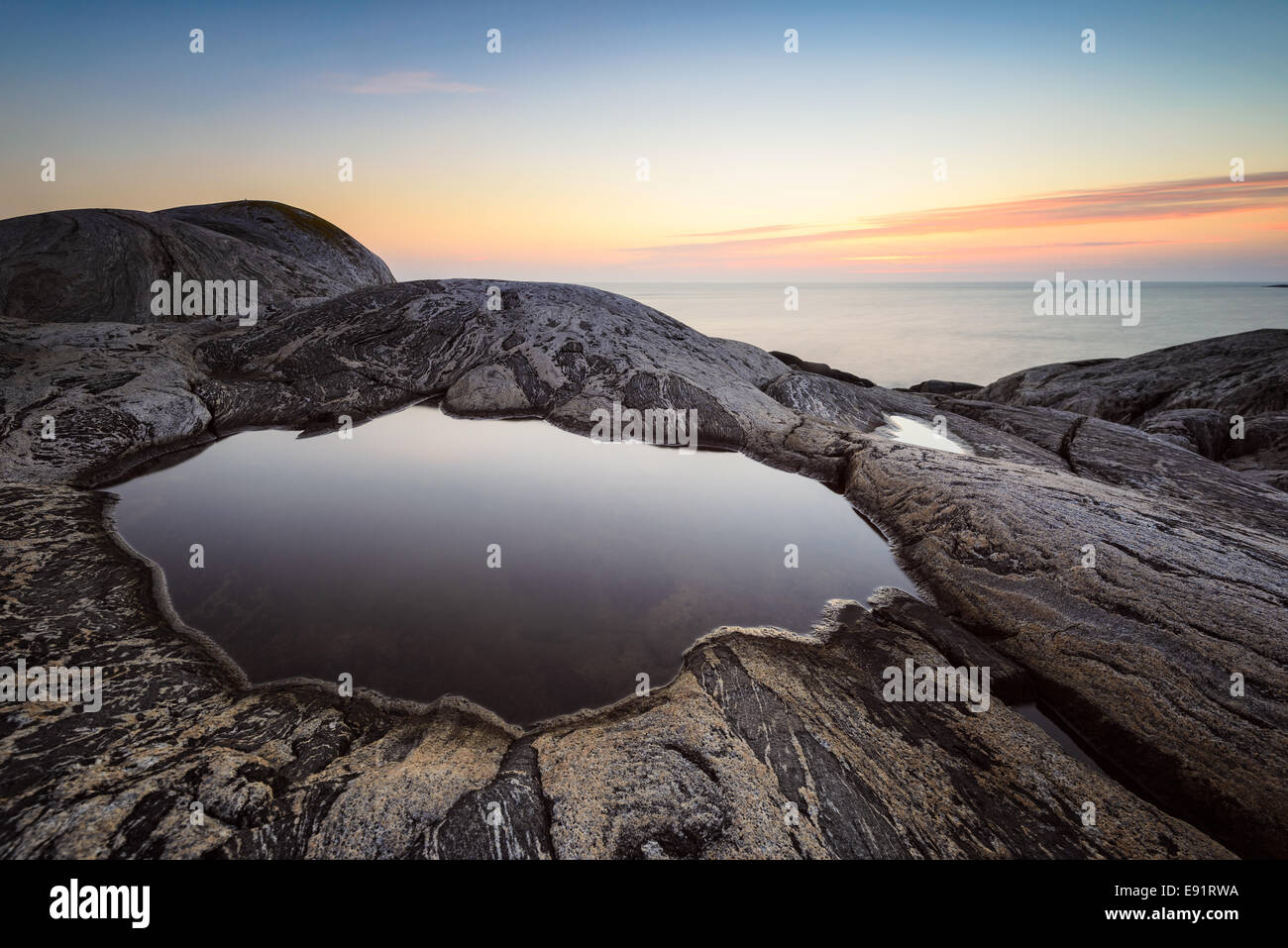 Smooth tide pool surrounded by rock at sunset Stock Photo