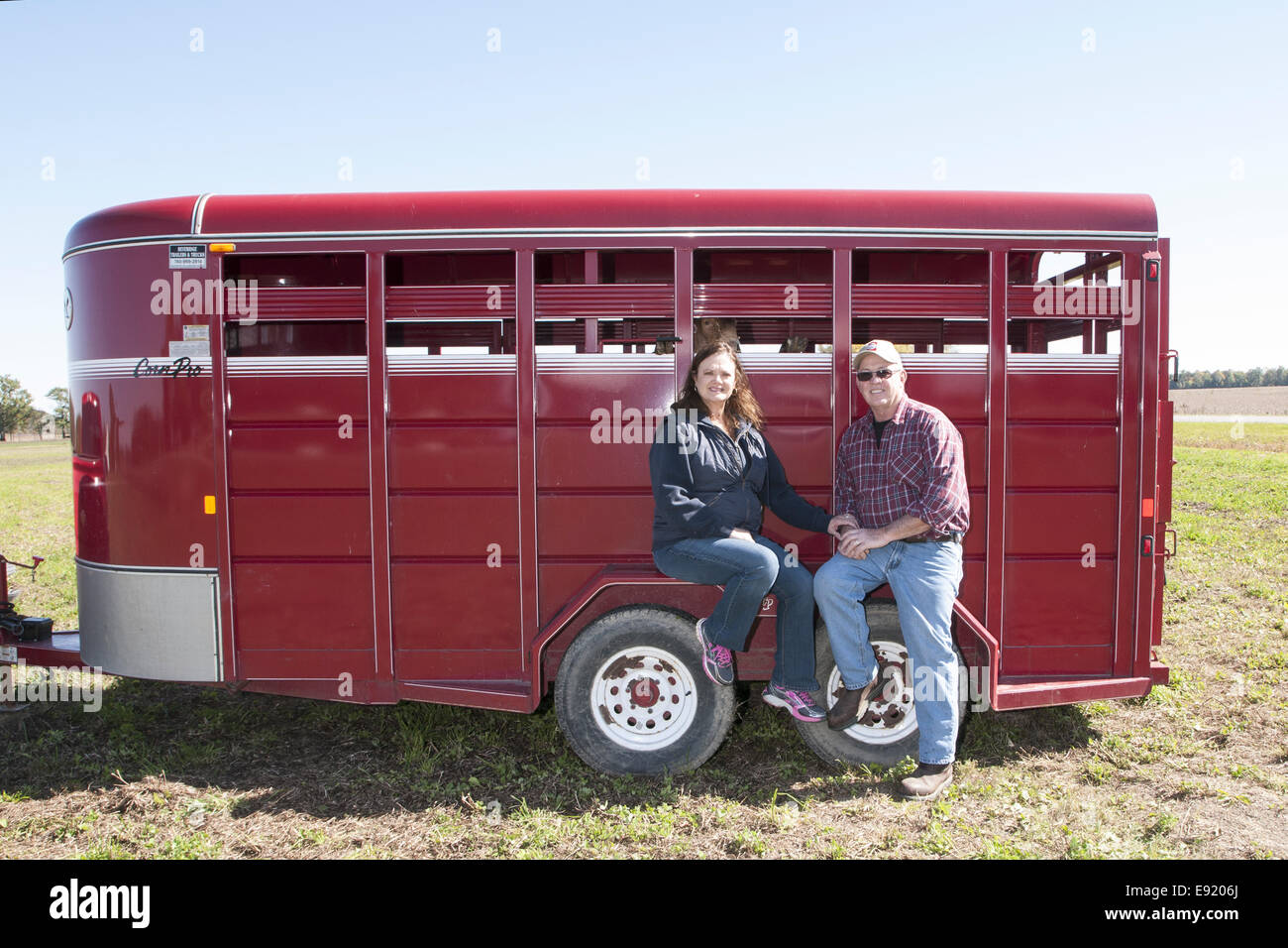 50-60 man and woman sitting on the wheel well cover of a red stock trailer. Stock Photo