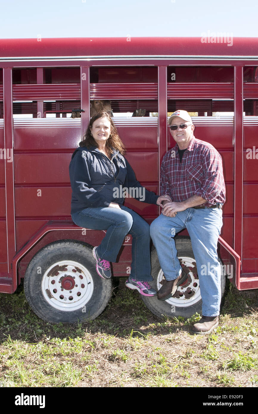 50-60 man and woman sitting on the wheel well cover of a red stock trailer. Stock Photo