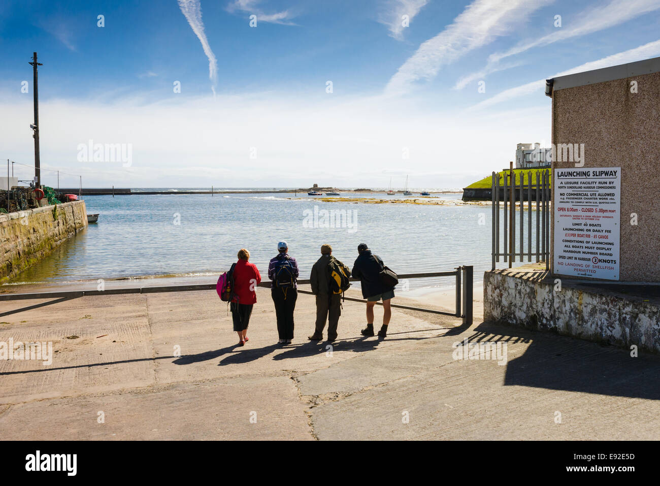Four daytrippers waiting looking out to sea on a clear day. Seahouses harbour, harbor Northumberland. Stock Photo