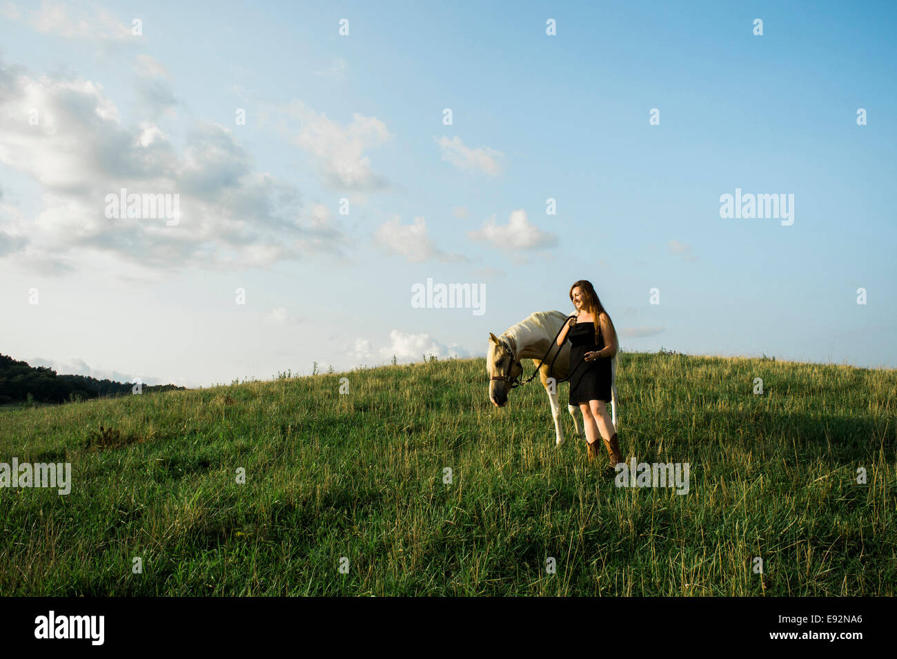 Young Women in Black Dress Walking Horse Across Field Stock Photo