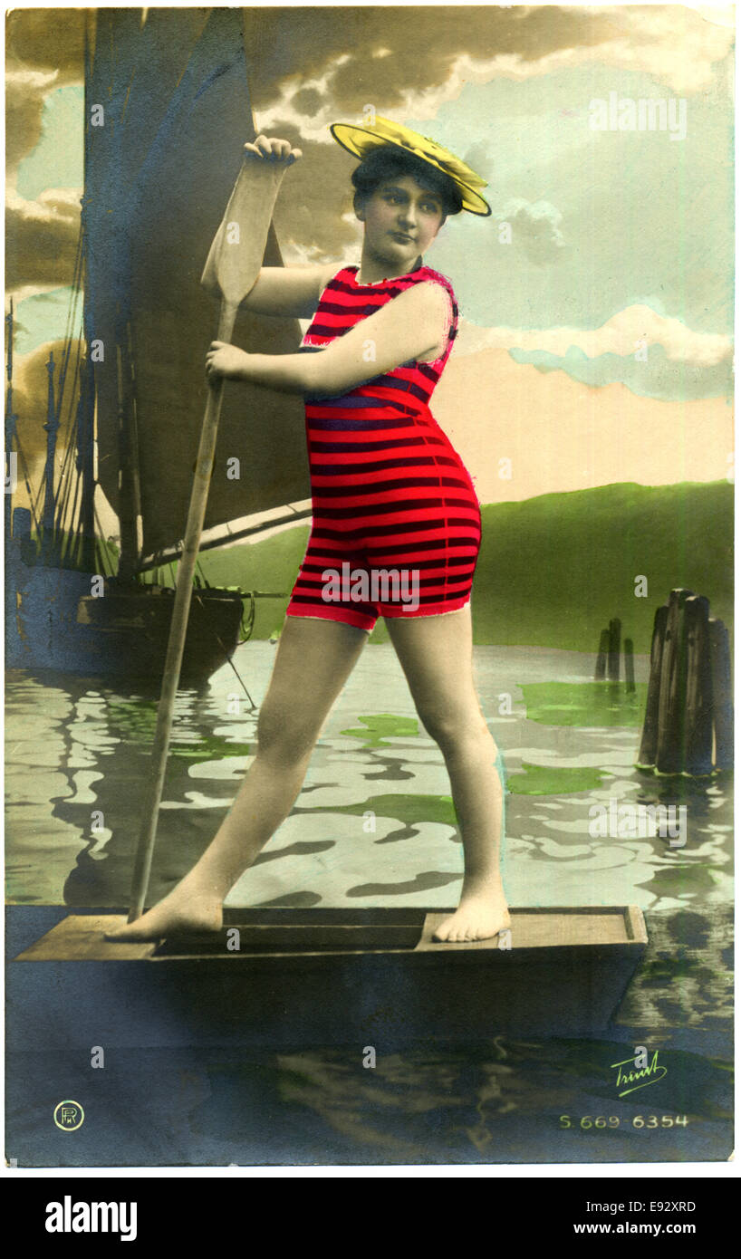 Woman in Red Striped Swimsuit Standing on Boat with Oar, Hand-Colored, Postcard, circa early 1900's Stock Photo