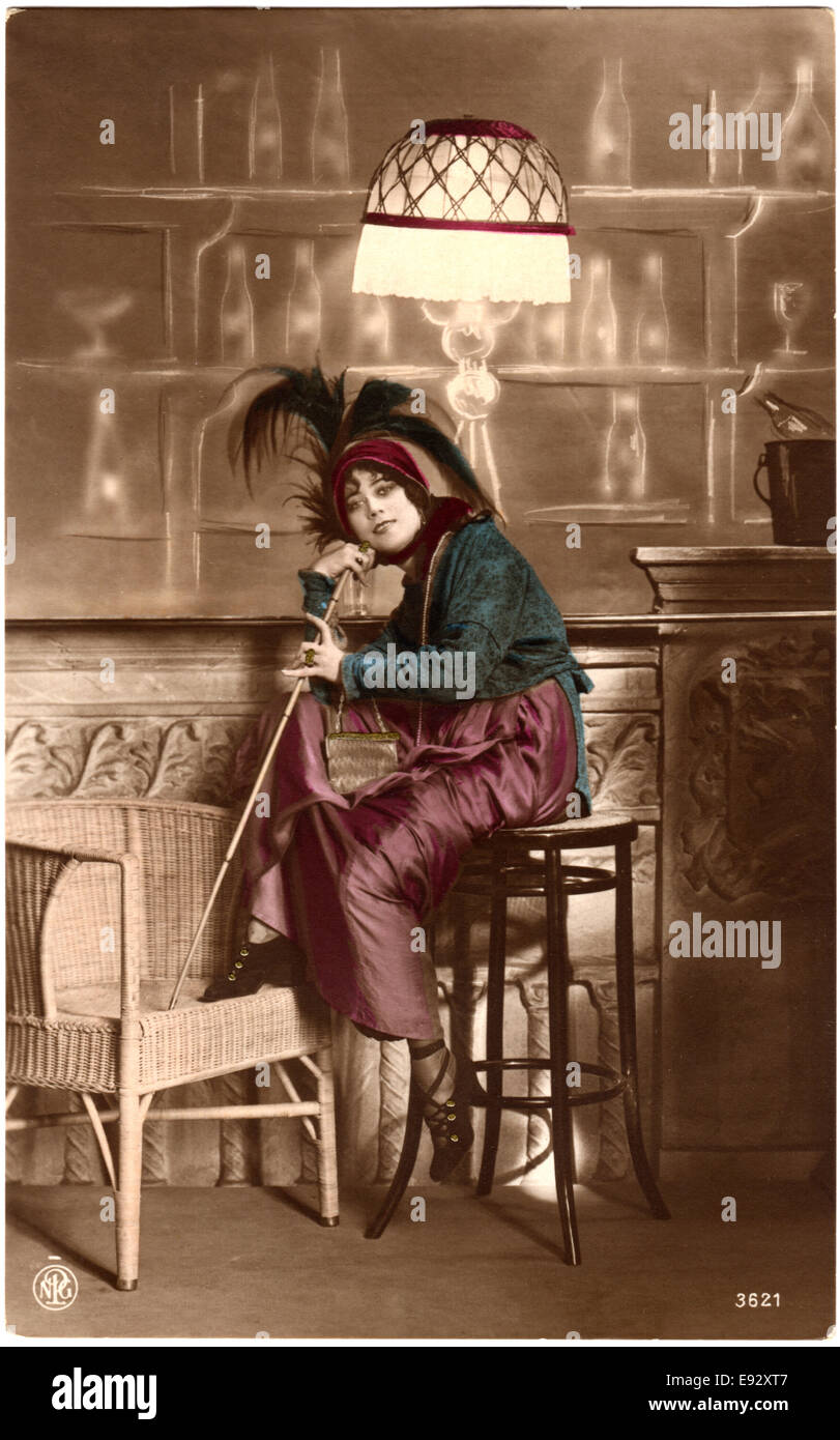 Smiling Woman Wearing Plume Hat Seated on Barstool and Holding a Walking Cane, Hand-Colored Postcard, circa 1910's Stock Photo