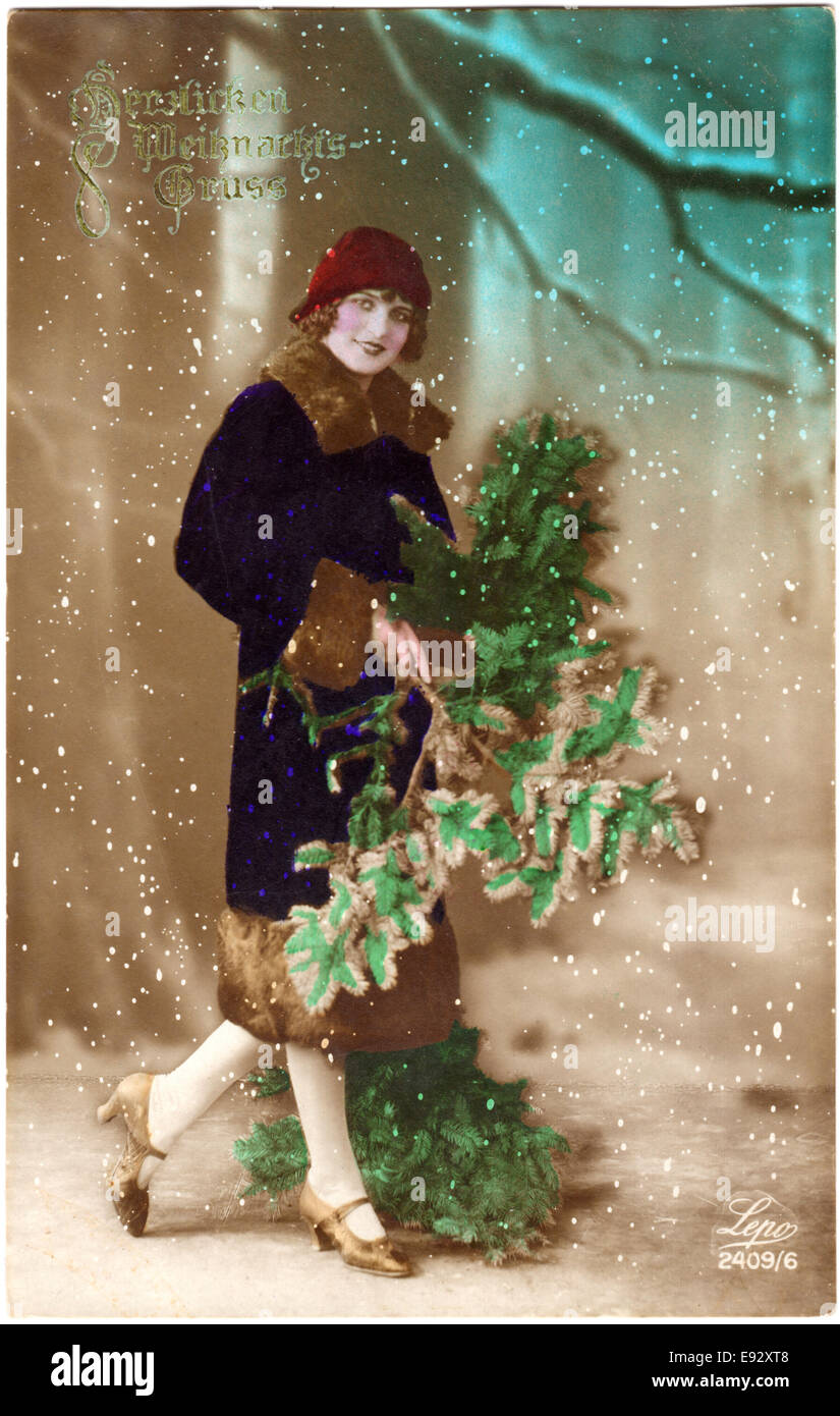 Smiling Woman in Red Hat and Blue Coat Holding Green Boughs, Hand-Colored Christmas Postcard, circa 1920's Stock Photo