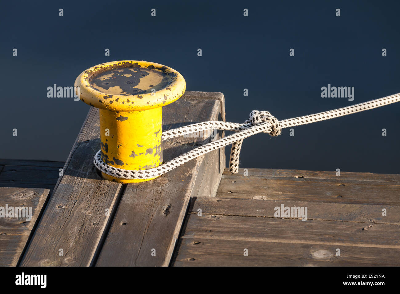 Yellow mooring bollard with nautical rope on wooden pier Stock Photo