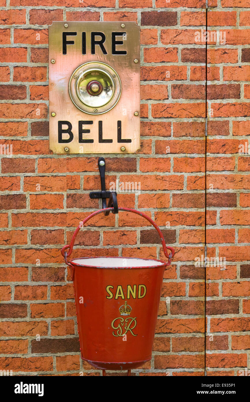 Fire bell and sand bucket attached to a red brick wall Stock Photo