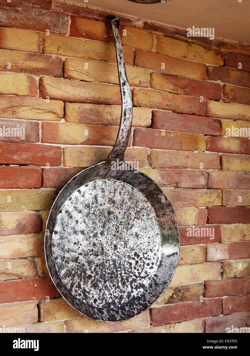 Antique frying pan hanging on brick wall. Stock Photo