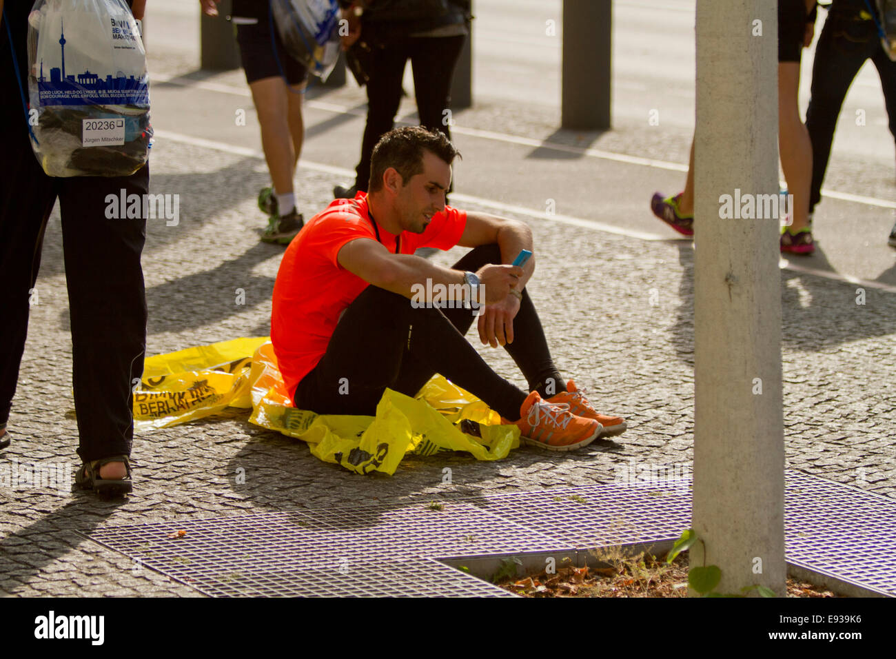 Marathon runner sat on floor with people walking Stock Photo