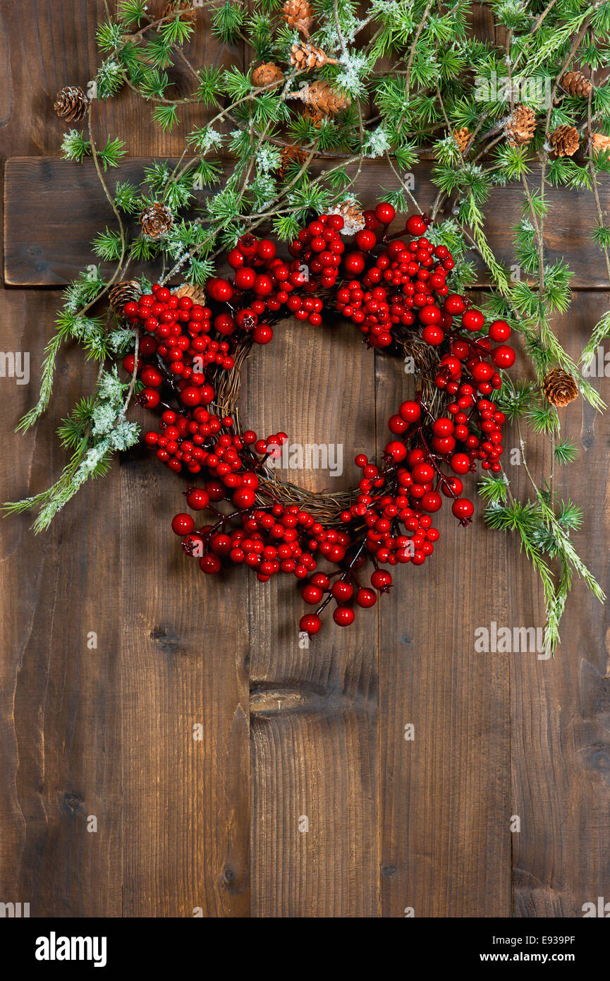 christmas tree branches and wreath from red berries over rustic wooden background. festive decoration Stock Photo
