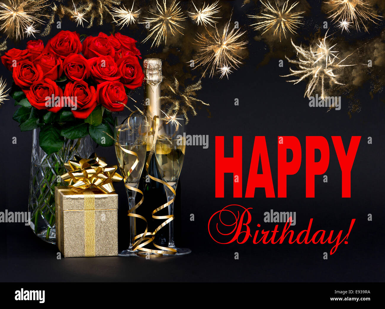 red roses, bottle of champagne, golden gift with beautiful fireworks on black background. card concept with sample text Happy Bi Stock Photo