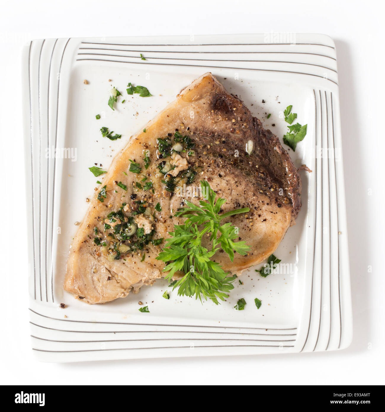 Cooked peppered swordfish steak with a parsley and garlic butter sauce on a plate viewed from above Stock Photo