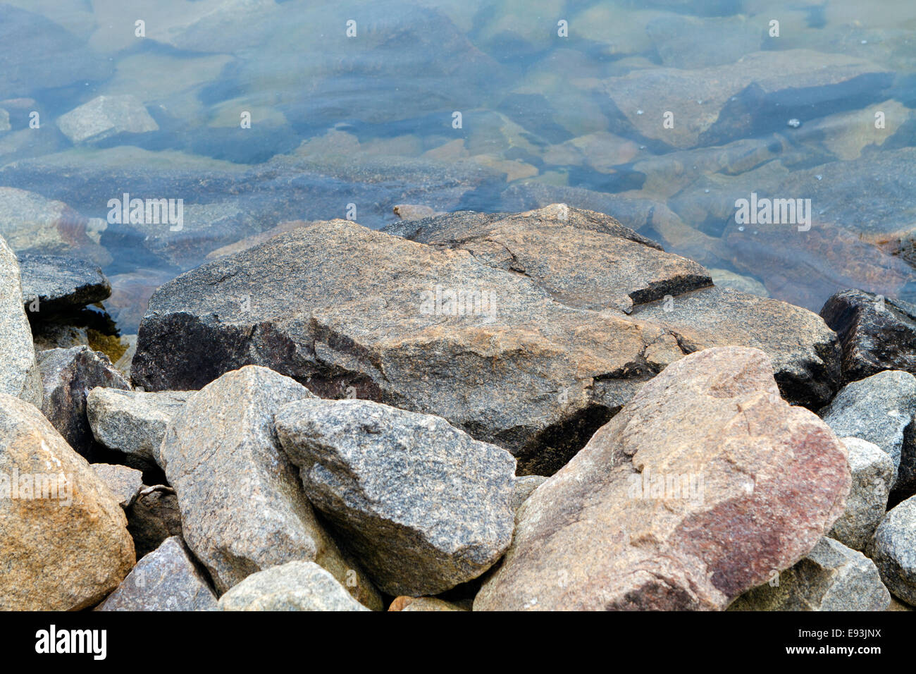 A pile of granite rock boulders along a fresh water lake shoreline. Stock Photo
