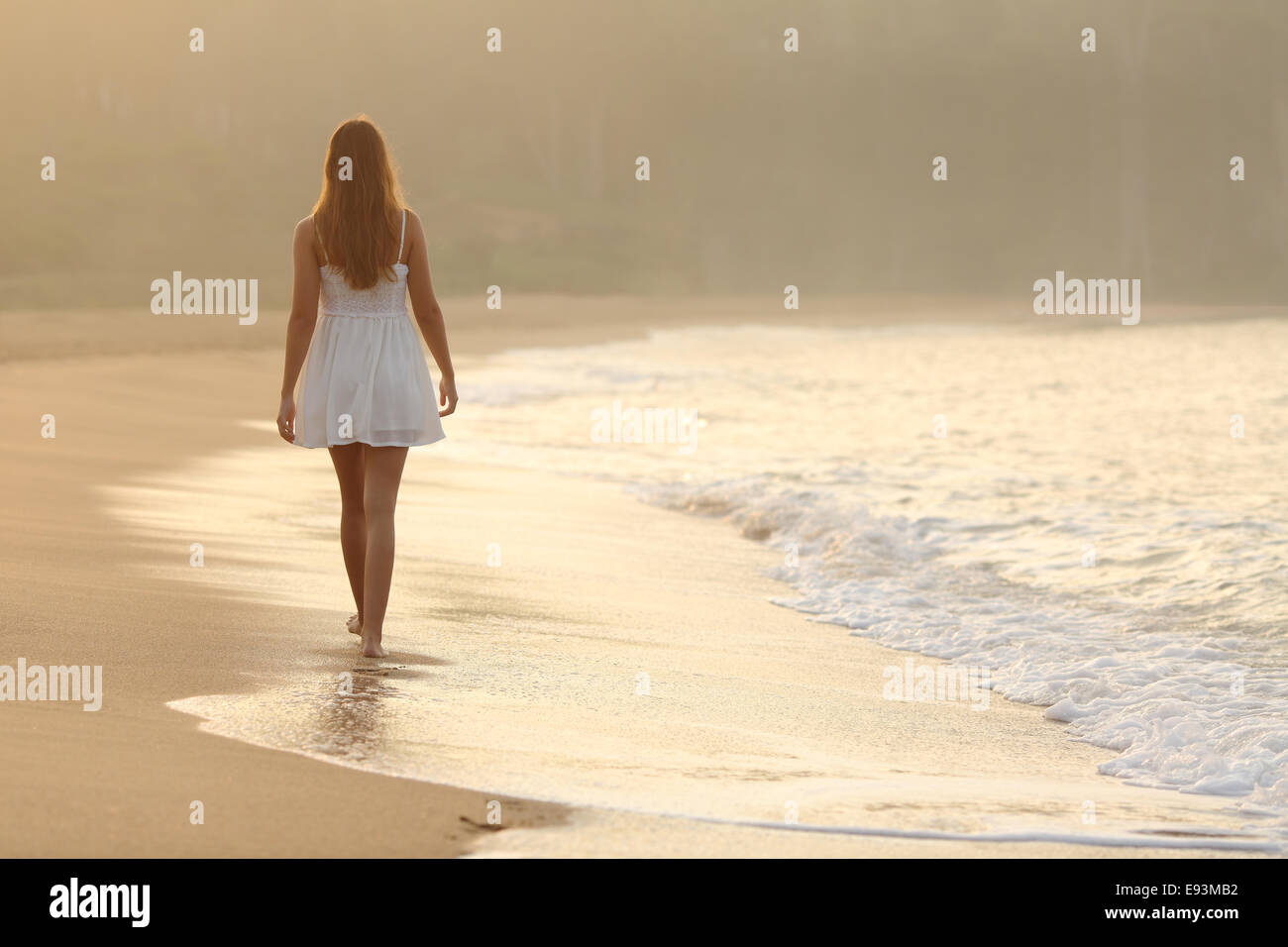 Back view of a woman walking on the sand of the beach at sunset Stock Photo