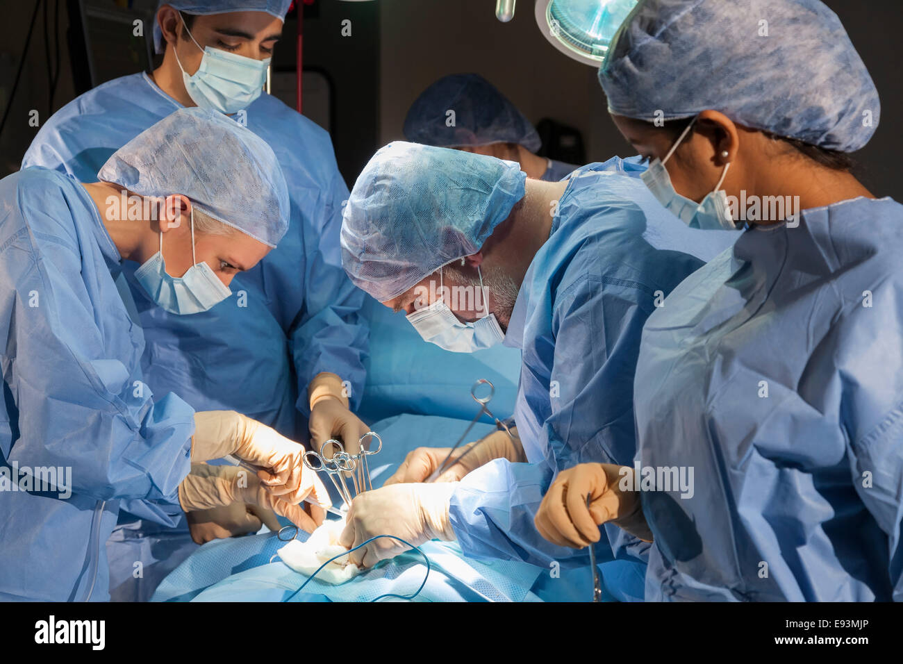 A team of interracial medical doctors male & female surgeons in surgery operating on a patient using different medical equipment Stock Photo