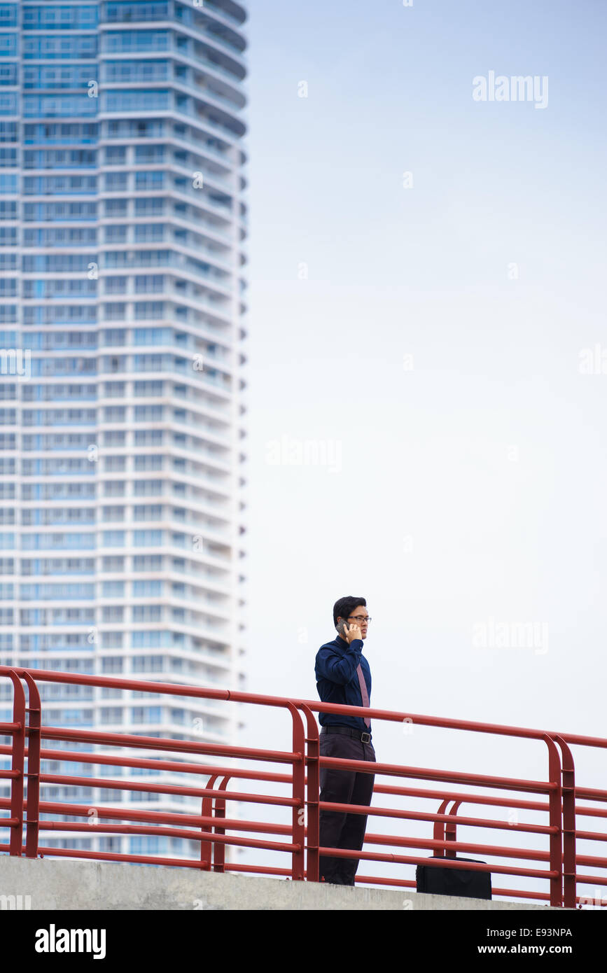Portrait of chinese businessman standing on bridge in Panama city with skyline in background, answering phone call Stock Photo