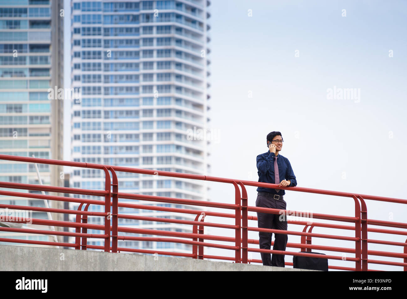 Portrait of chinese businessman standing on bridge in Panama city with skyline in background, answering phone call Stock Photo