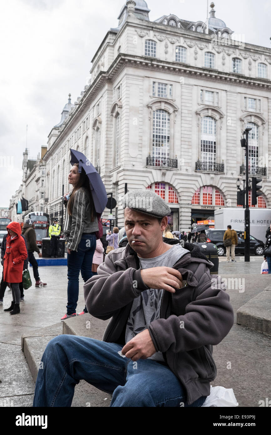 Man in a flat cap make a roll up cigarette in London's Piccadilly Circus Stock Photo