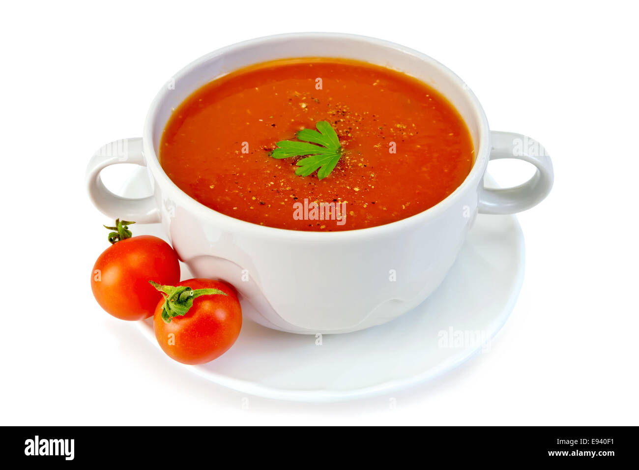Tomato soup in a white bowl with parsley on a plate with tomatoes isolated on white background Stock Photo