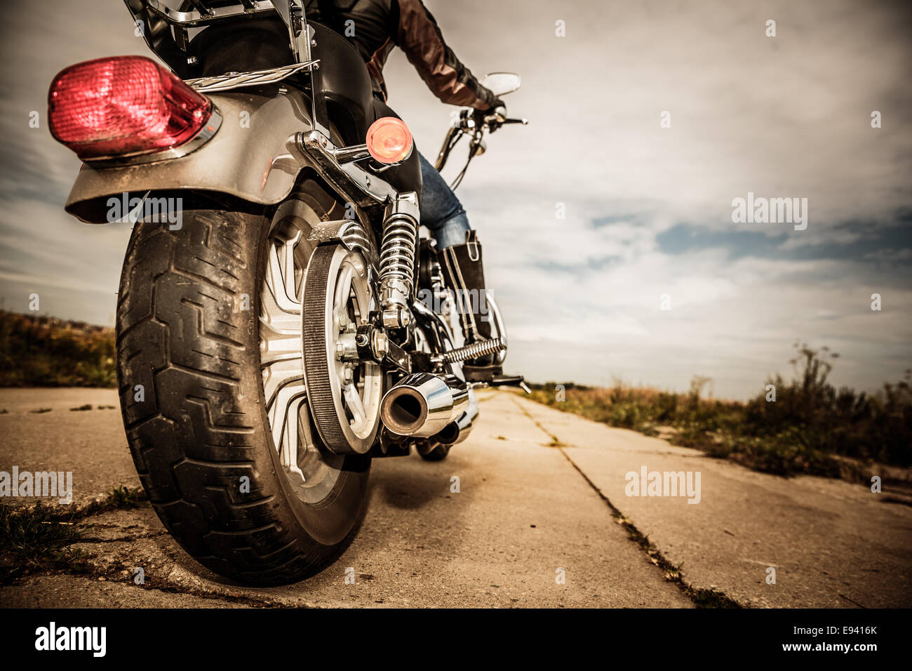 Biker girl riding on a motorcycle. Bottom view of the legs in leather boots. Focus on the rear wheel. Stock Photo