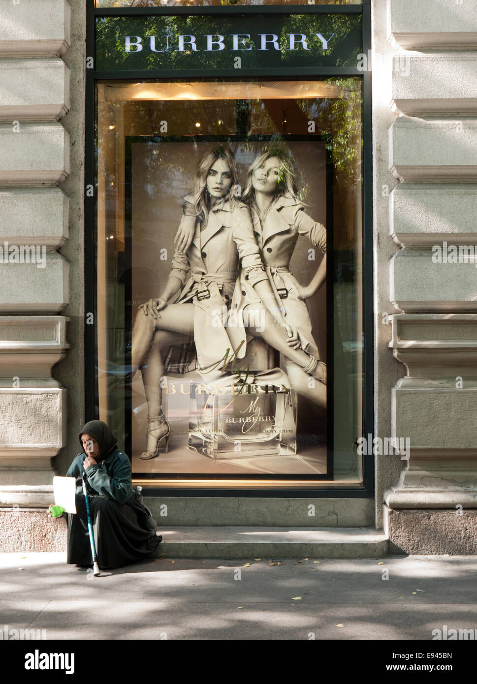 Beggar woman sitting in front of an elegant fashion store's window Stock Photo