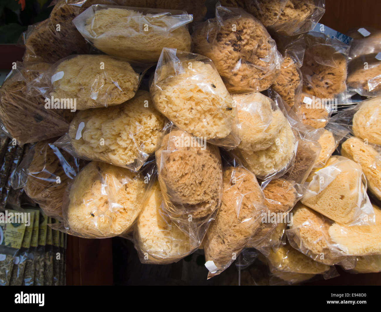 Numerous sponges in plastic wrapping, popular and useful souvenir for sale to tourists in the Greek islands, here a shop in Samos Stock Photo